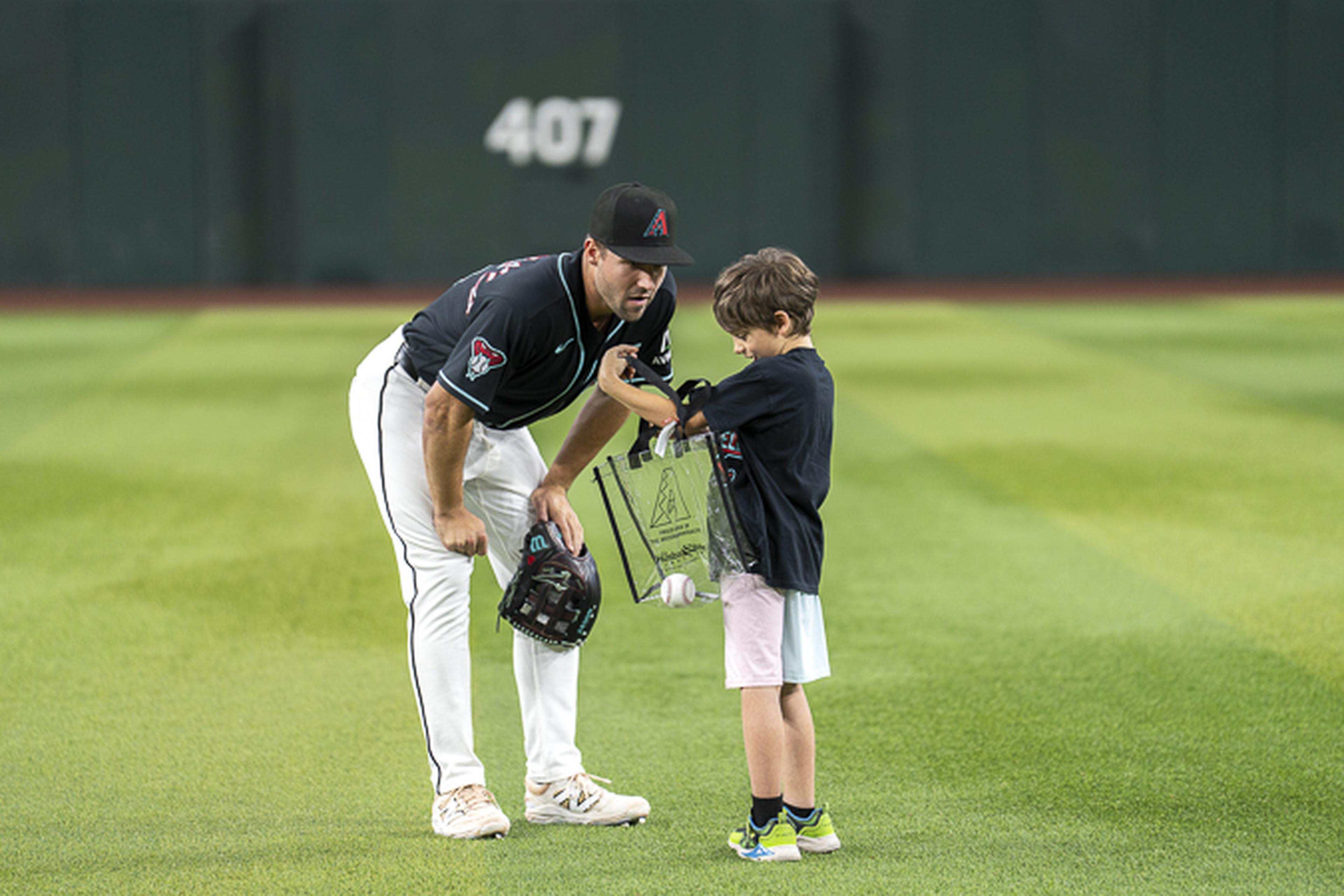 A Diamondbacks player with a glove chats with a young boy holding a clear bag and baseball on Chase Field in downtown Phoenix.