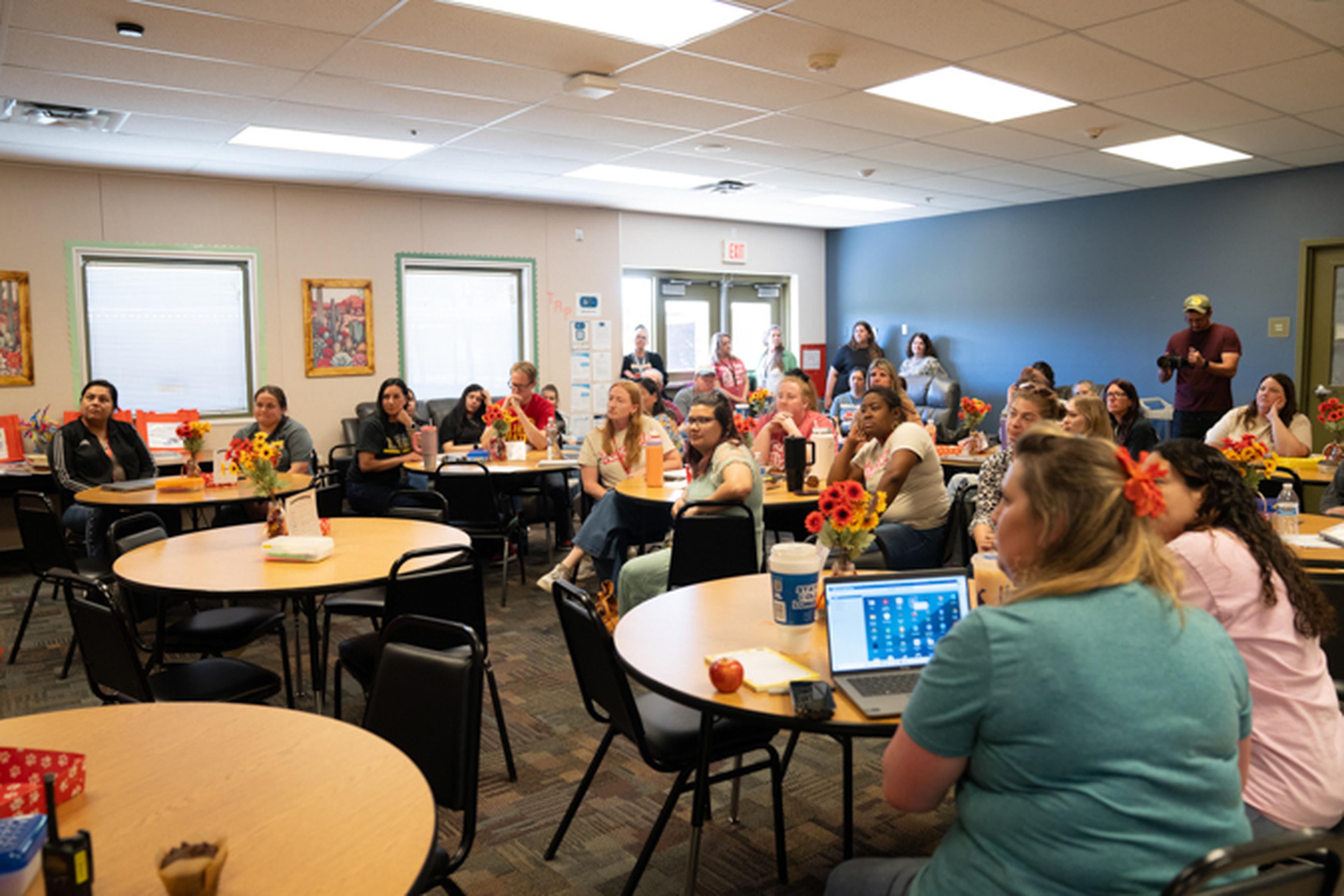 Ms. Shade's Sunrise Elementary faculty seated at round tables in a brightly lit room, attentively listening to a presentation.