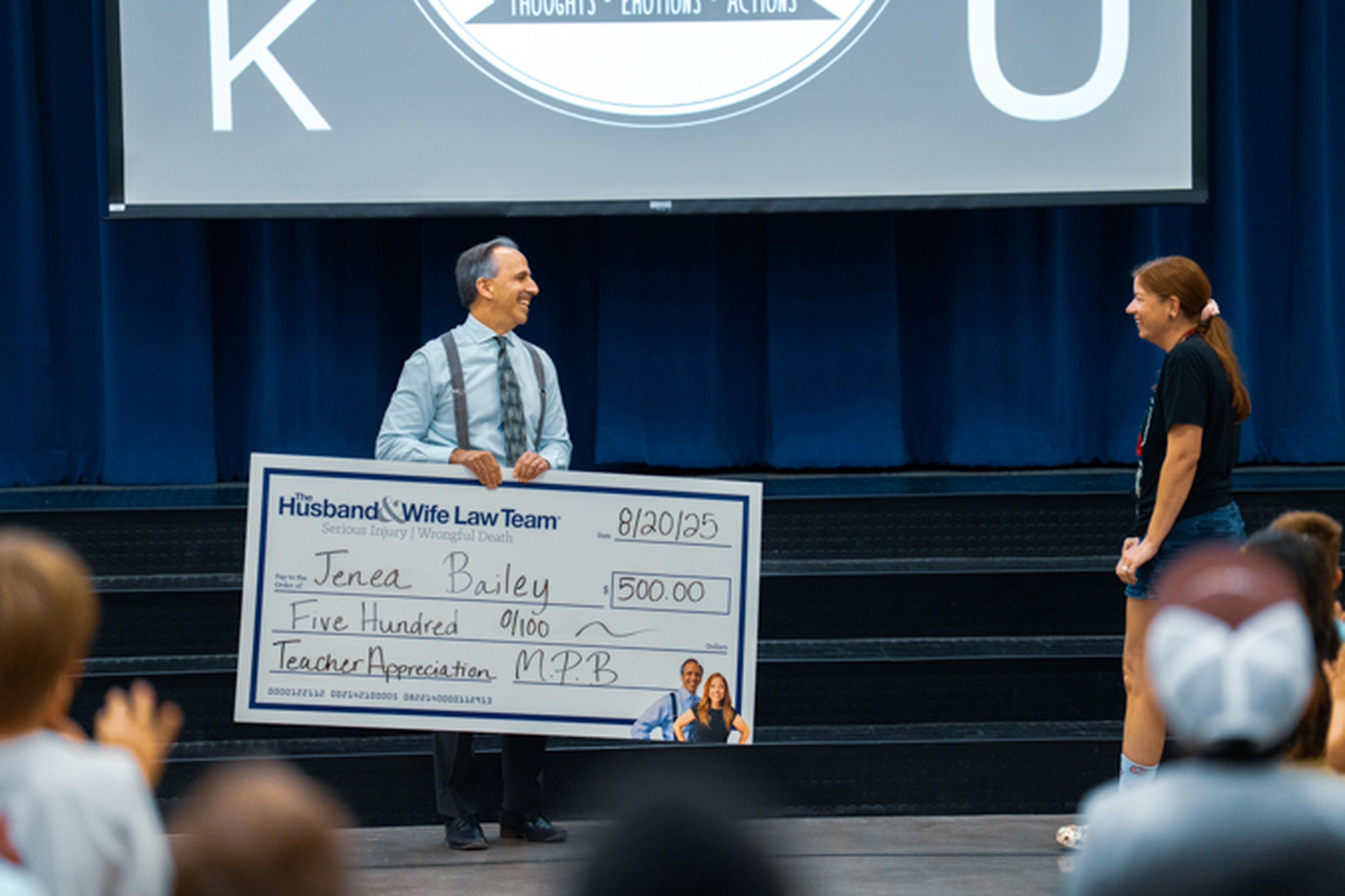 Mark Breyer holding the big check for Teacher Appreciation as Mrs. Bailey approaches