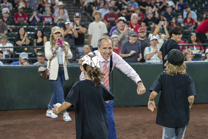 Mark Breyer of the Husband & Wife Law Team enthusiastically fist‑bumps two kids on Chase Field in downtown Phoenix as cheering spectators snap photos in the background.