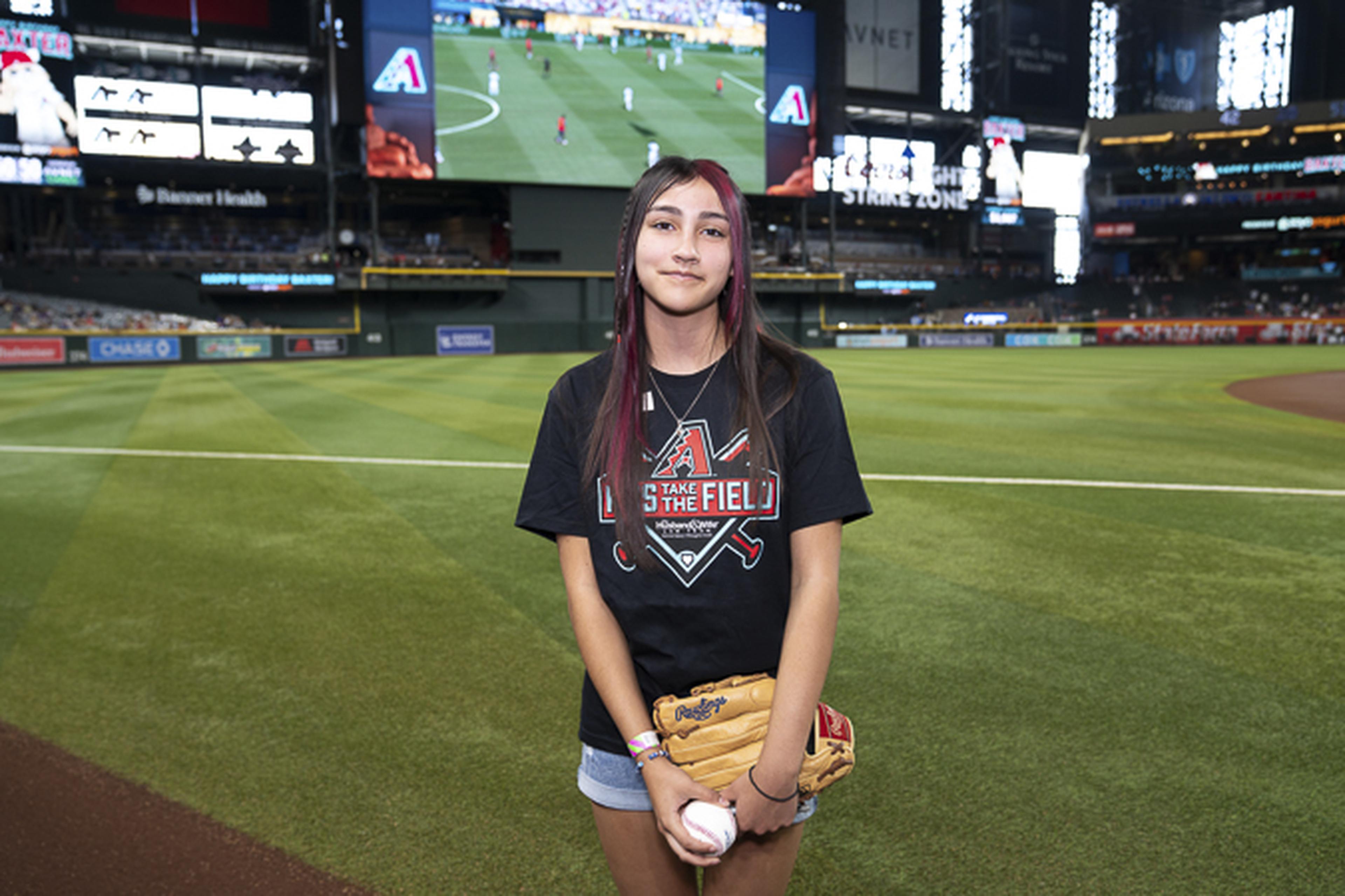 Dreaming of the big leagues, this young baseball fan stands proudly on Chase Field with glove and ball in hand, ready to chase her future on the diamond.