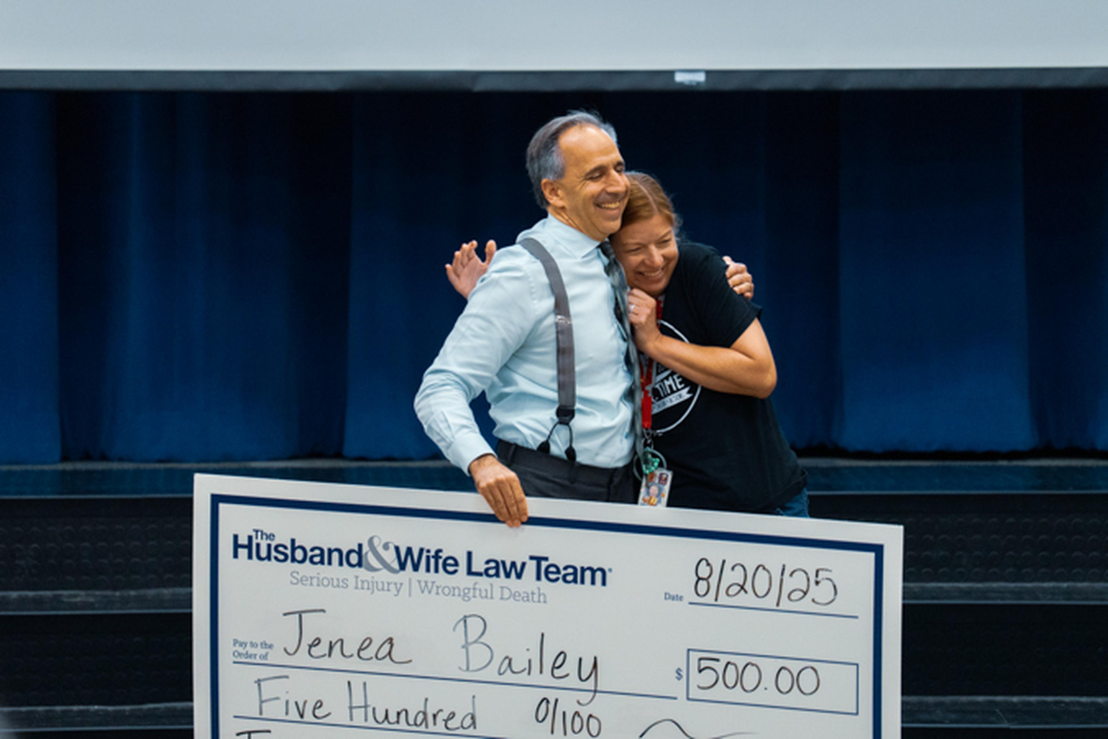 Mark Breyer receiving a hug from Teacher of the Month while holding the big check
