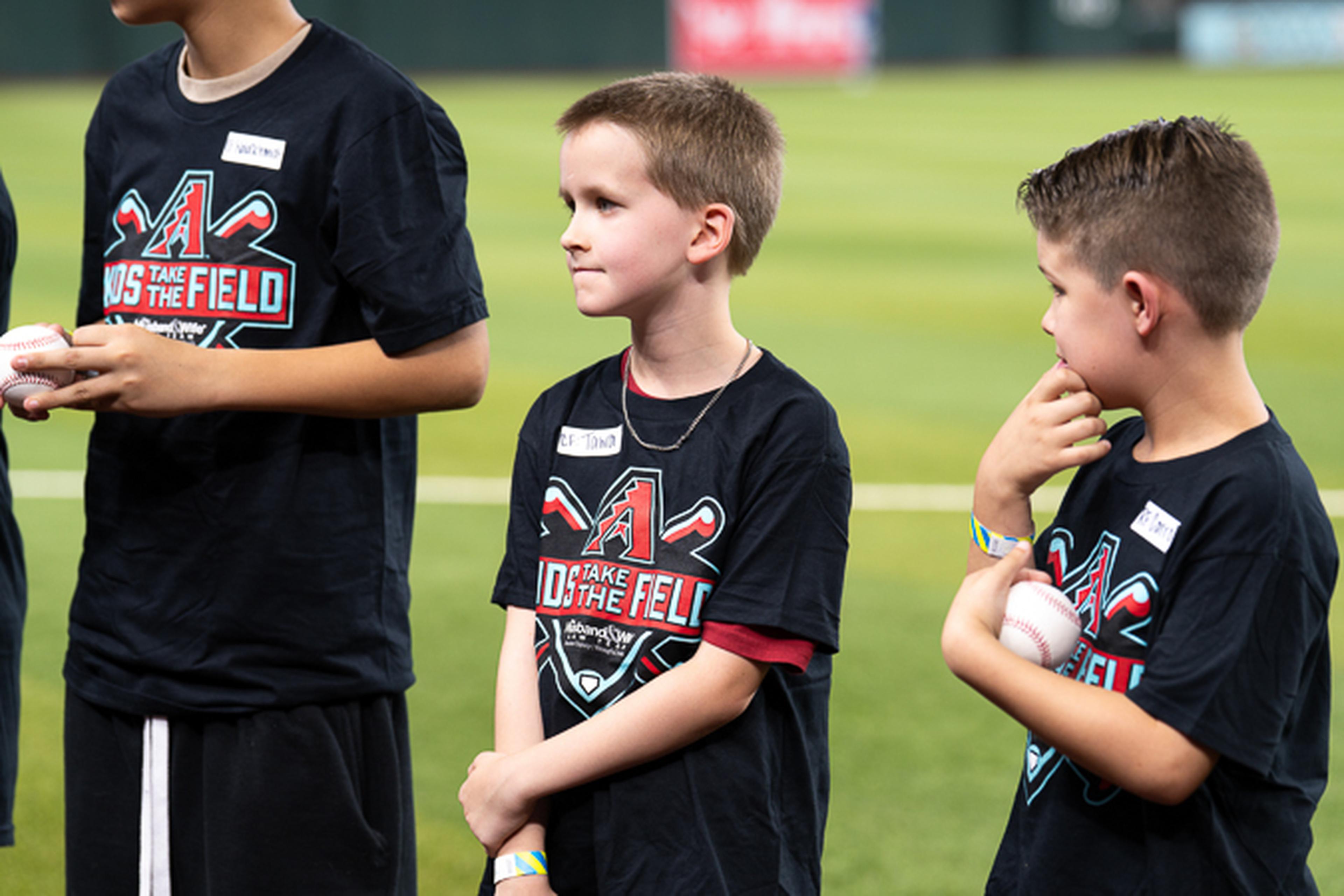 Three Kids Take the Field participants proudly hold their baseballs while posing together on the field during an unforgettable day at the ballpark.