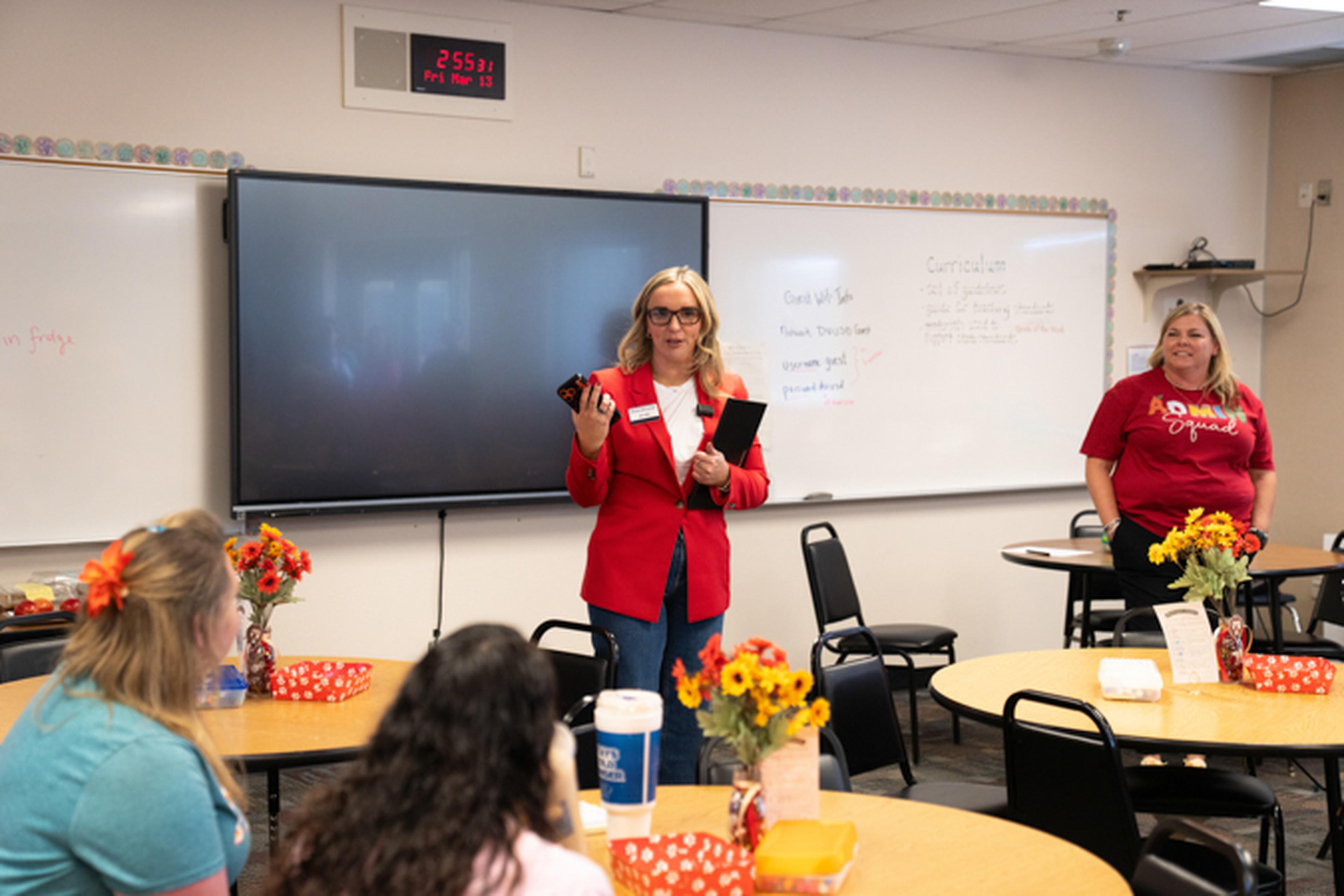Jen from The Husband & Wife Law Team speaks to seated attendees in a classroom with a large screen and decorated tables.