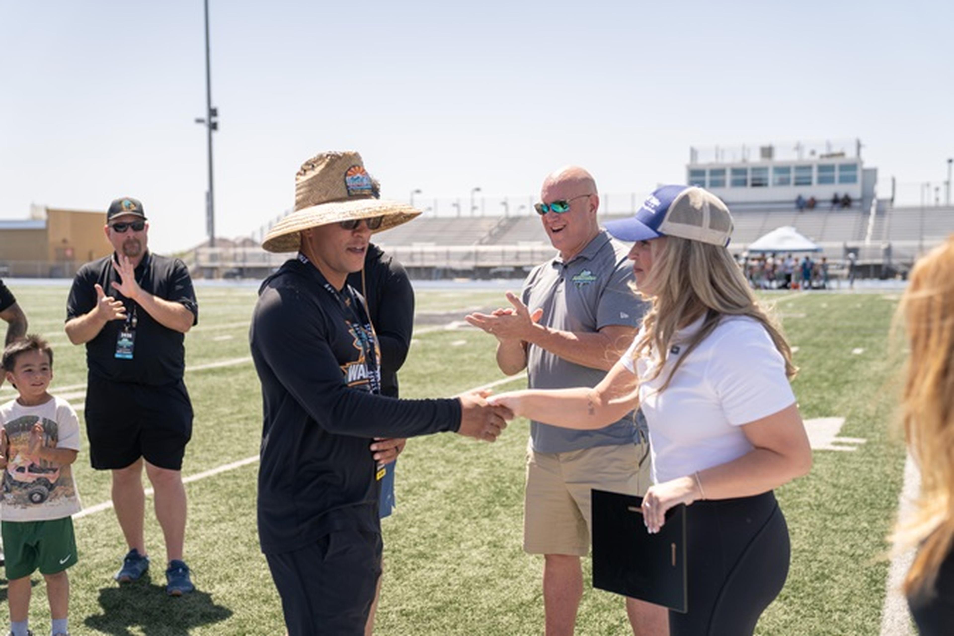 Jen from the Husband & Wife Law Team congratulates Coach Nino on the field as others clap under the clear Arizona sky.