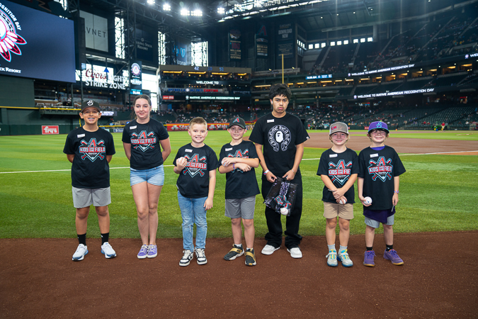 Kids Take the Field winners gather on Chase Field in matching tees and caps, each holding a baseball as they celebrate the moment.