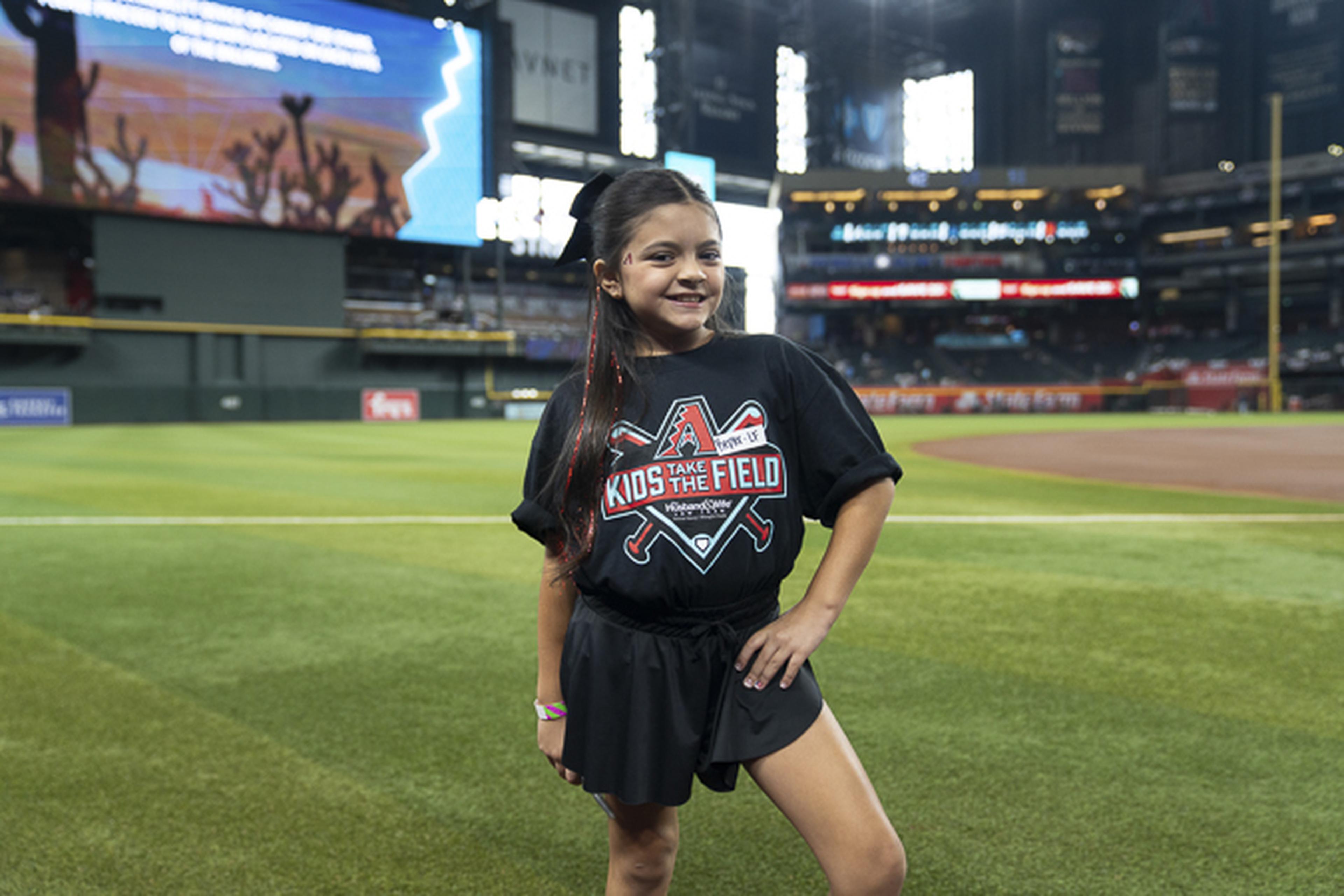 A young participant stands proudly on Chase Field before the National Anthem, enjoying a memorable Kids Take the Field experience at the ballpark.