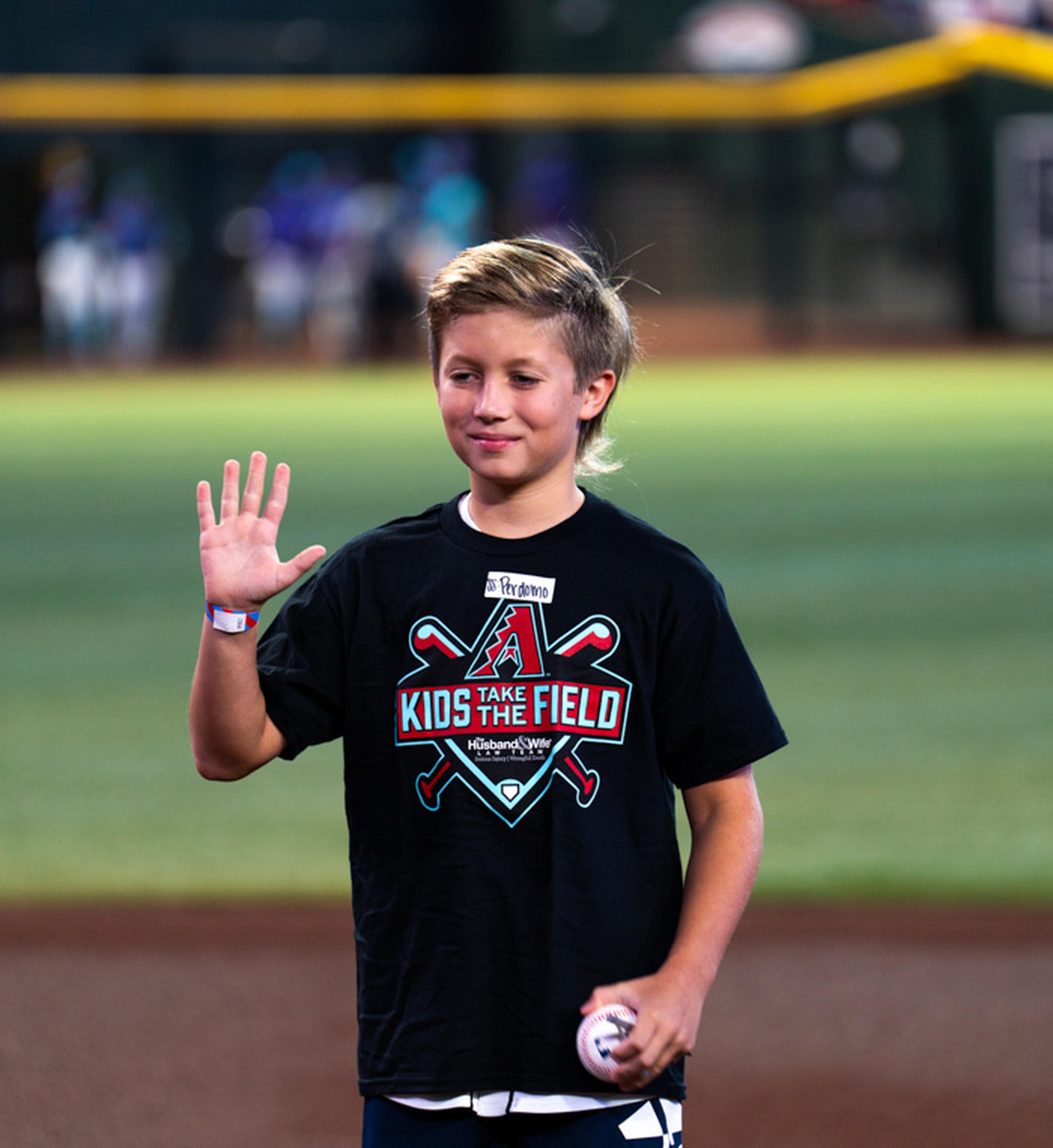 A young Kids Take the Field participant waves to the crowd while holding a baseball, soaking in every moment of his unforgettable experience on Chase Field.