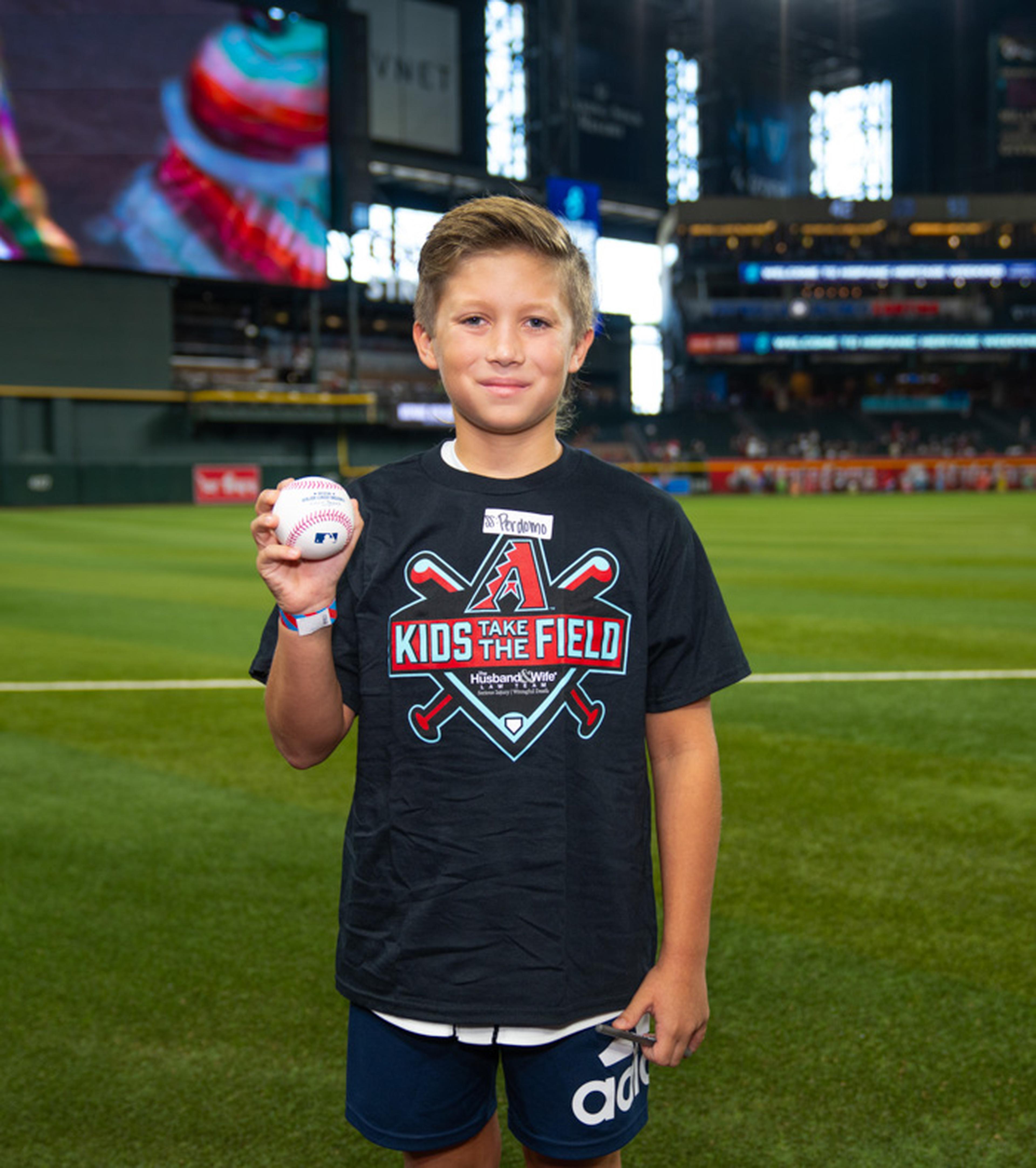 A young Kids Take the Field participant proudly holds a signed baseball on Chase Field, creating a lasting memory during a special day at the ballpark.