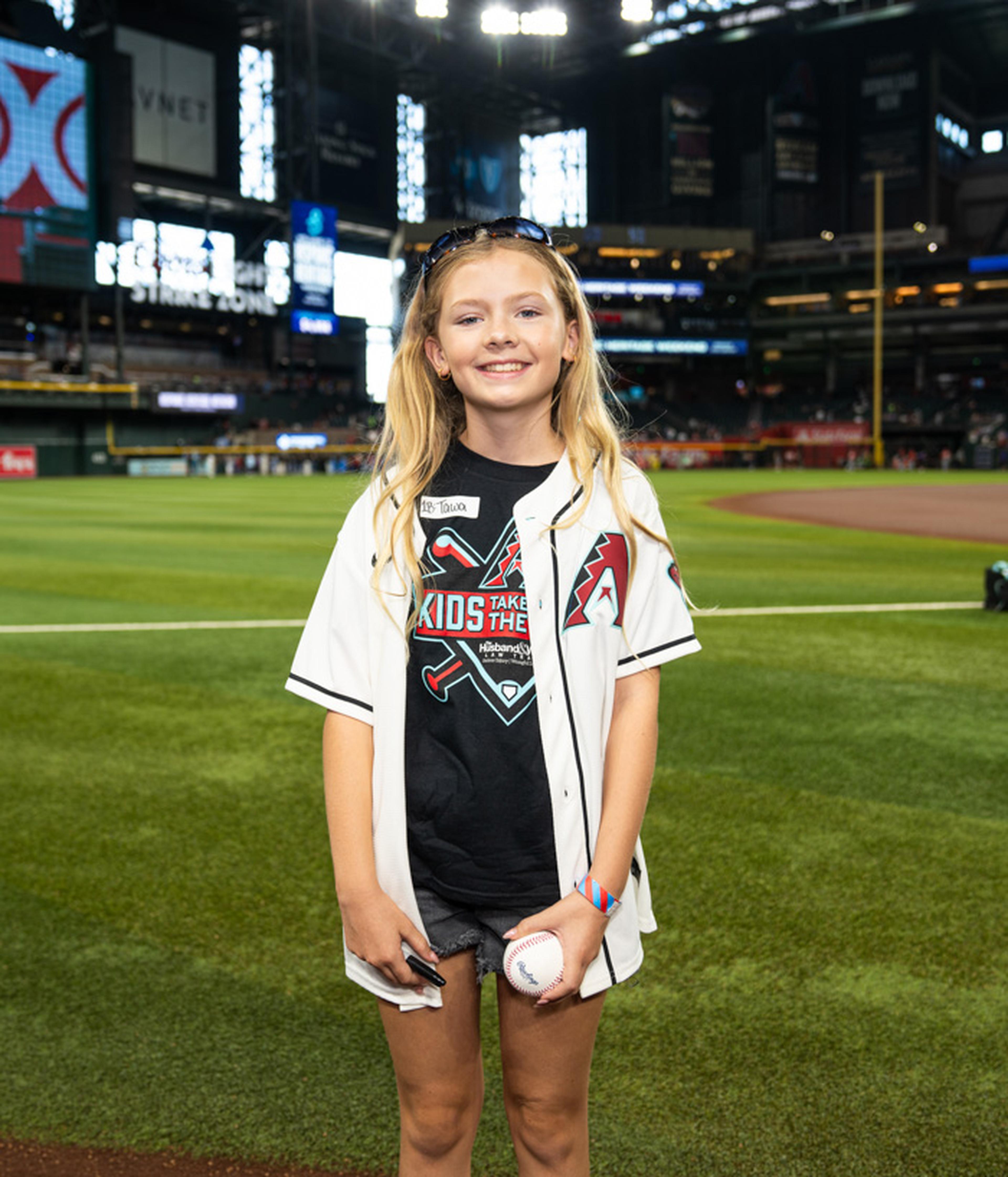 With a baseball in hand and a smile on her face, a young fan celebrates her special Kids Take the Field moment on the field at the home of the Arizona Diamondbacks.