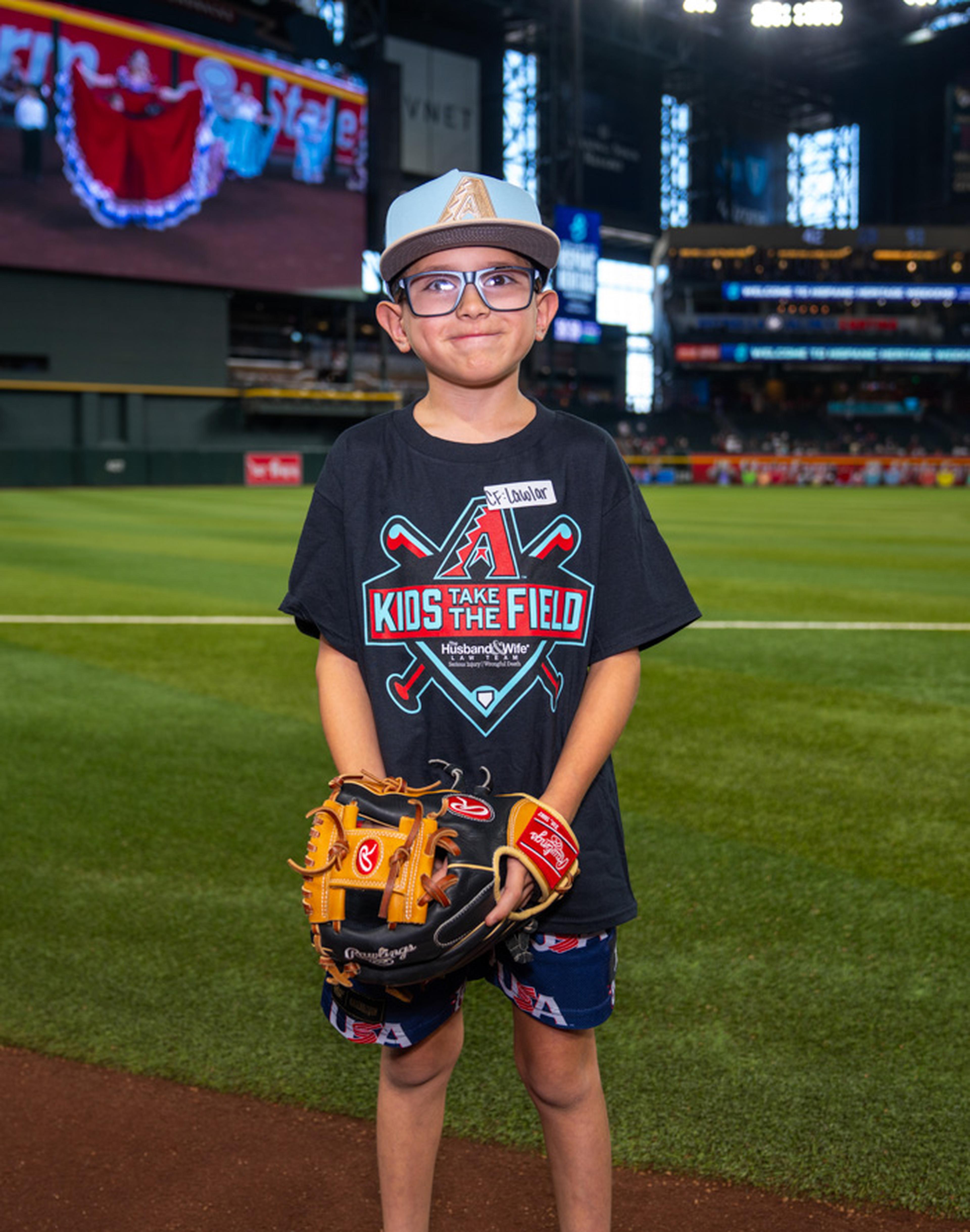 Wearing his Kids Take the Field shirt and baseball cap, a young fan smiles on the field as he takes in the excitement of a once-in-a-lifetime ballpark experience.