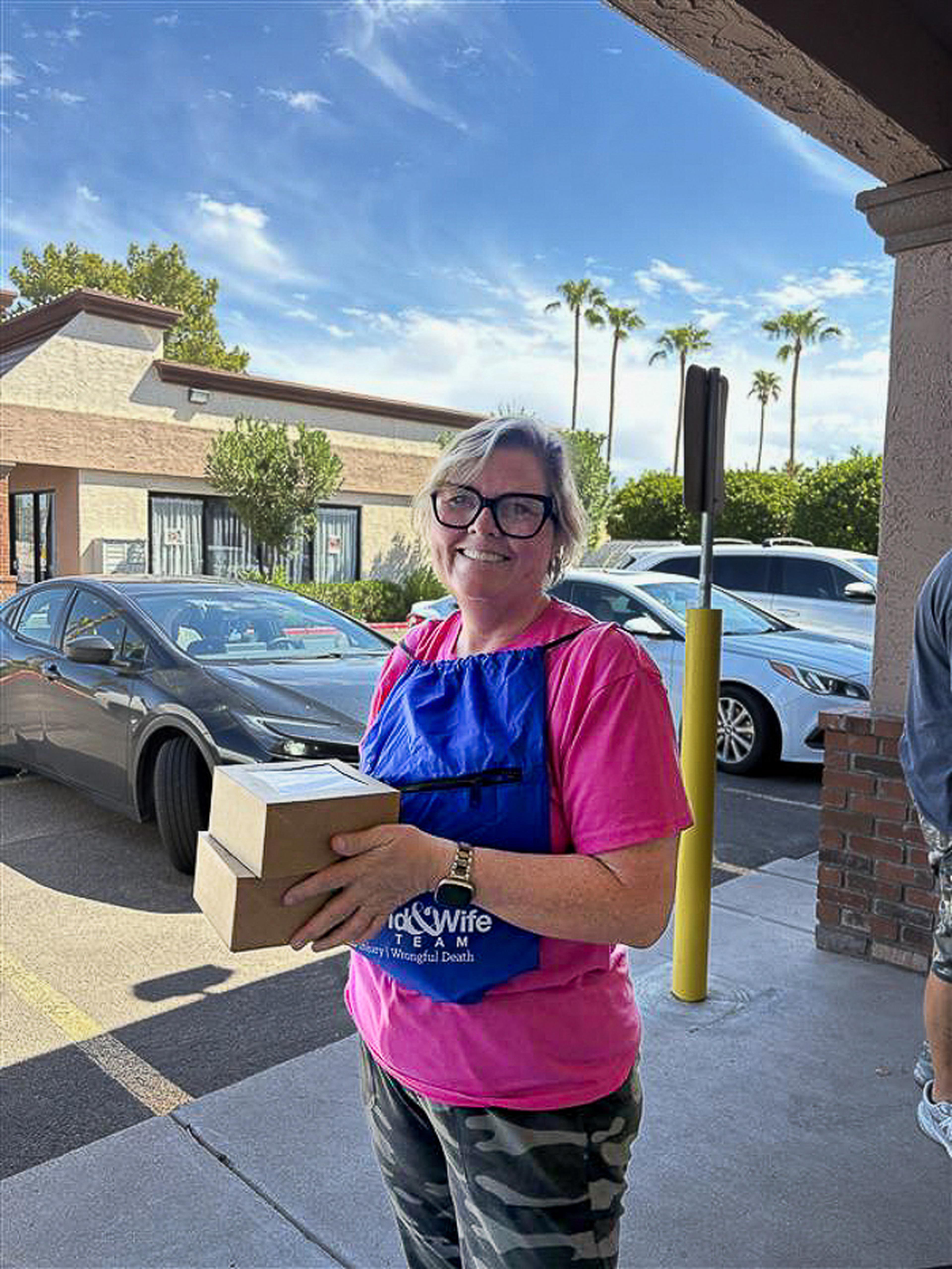 A smiling attendee holds bakery boxes outside Quiches & Pies Bakery during a Husband & Wife Law Team HEART event, enjoying local treats and community connection.