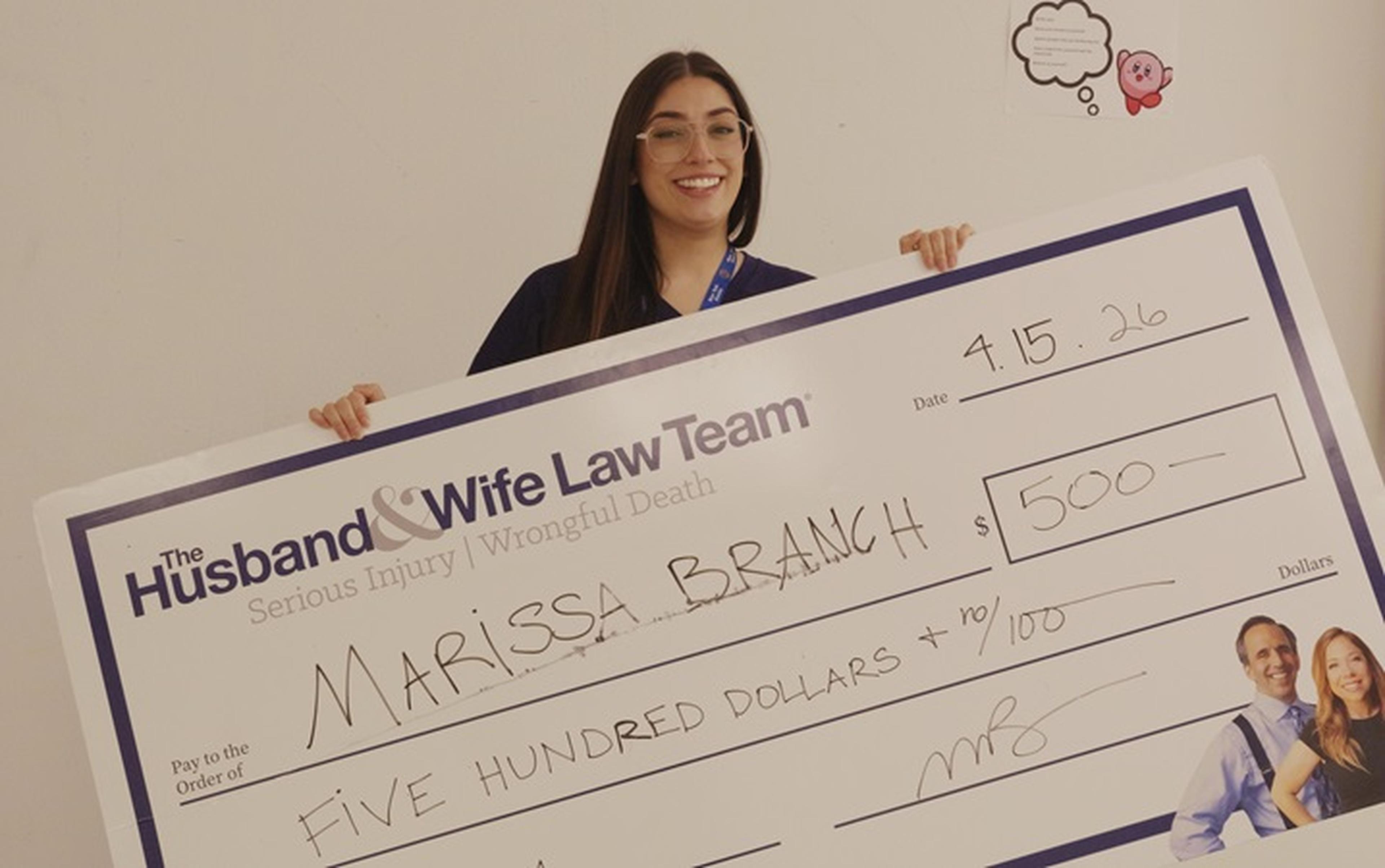 Ms. Branch holding a large novelty check for $500 from The Husband and Wife Law Team