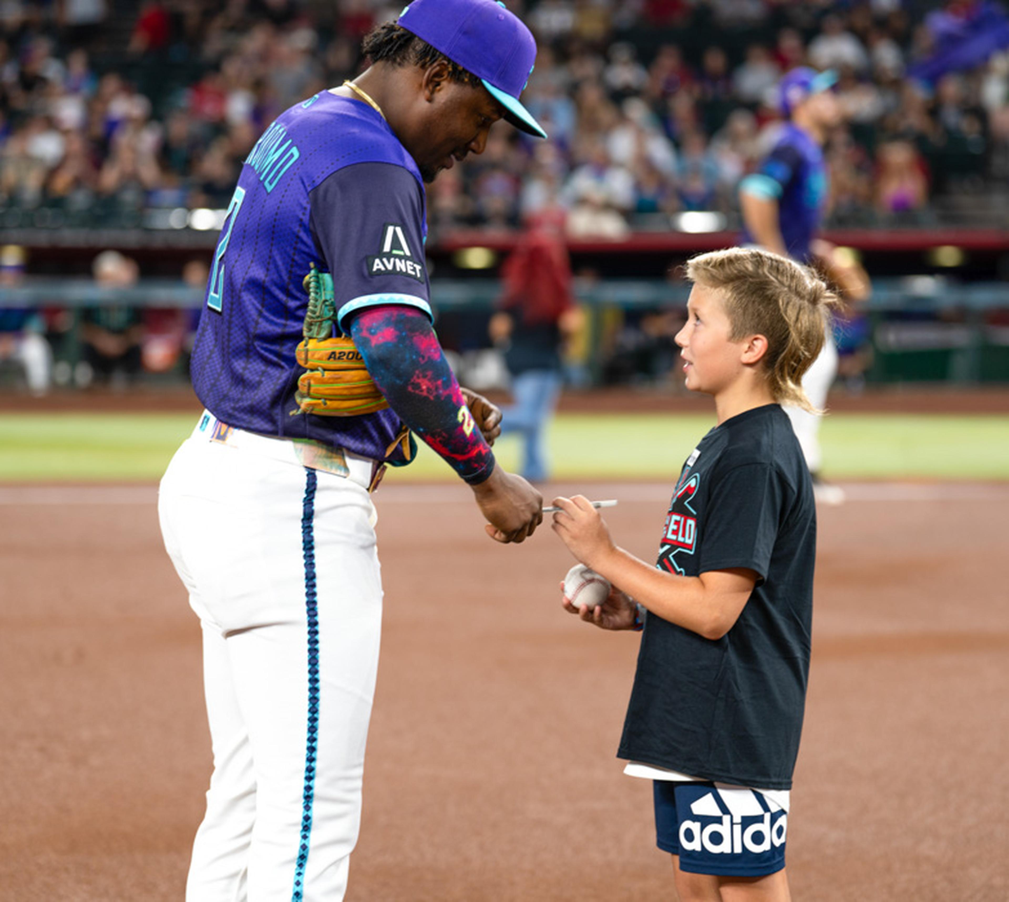 An Arizona Diamondbacks player signs a baseball for a young fan on the field, creating a once-in-a-lifetime memory during an unforgettable Kids Take the Field experience.
