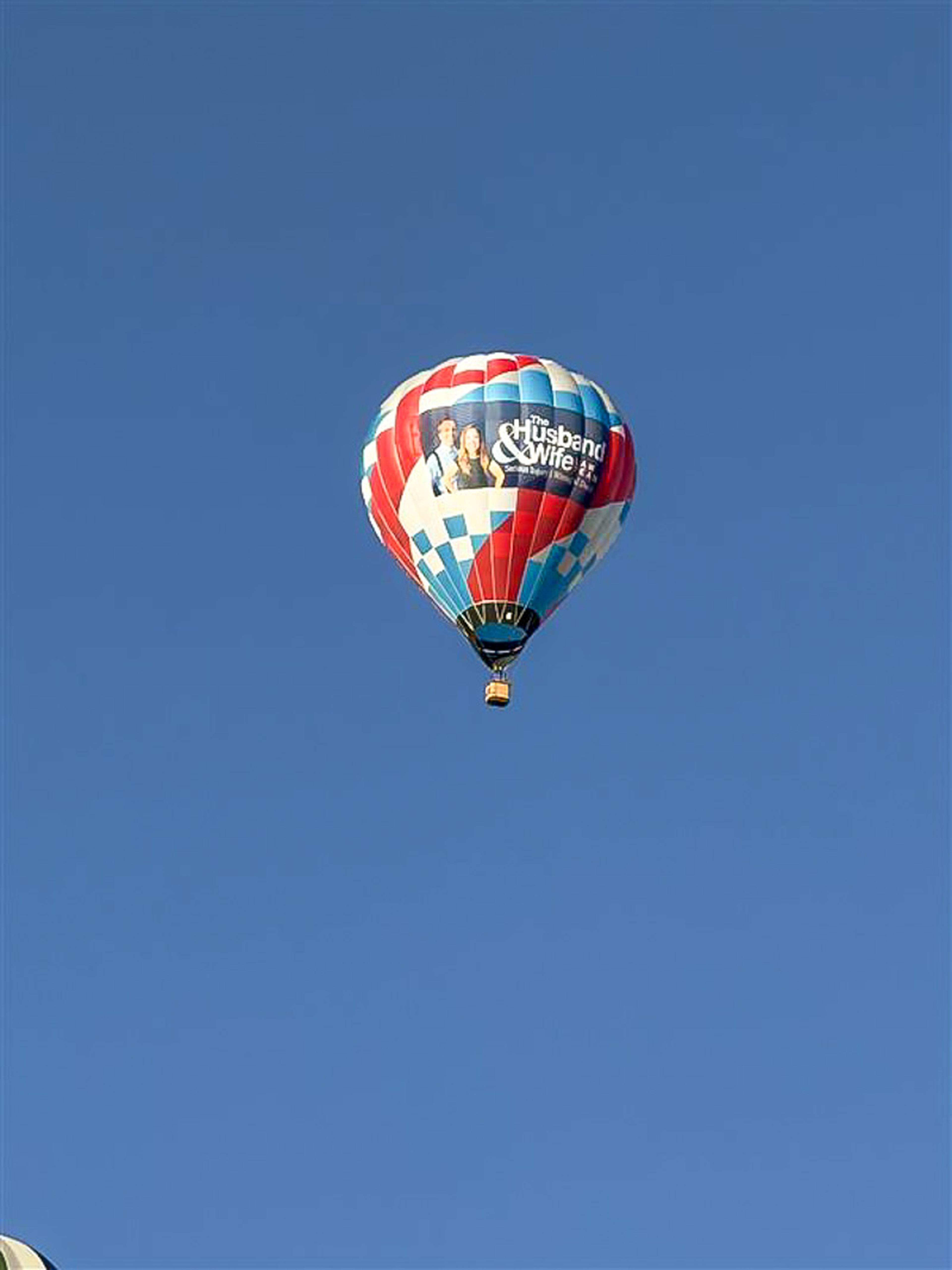 The Husband & Wife Law Team hot air balloon soars high against the bright blue Albuquerque sky during the Balloon Fiesta.
