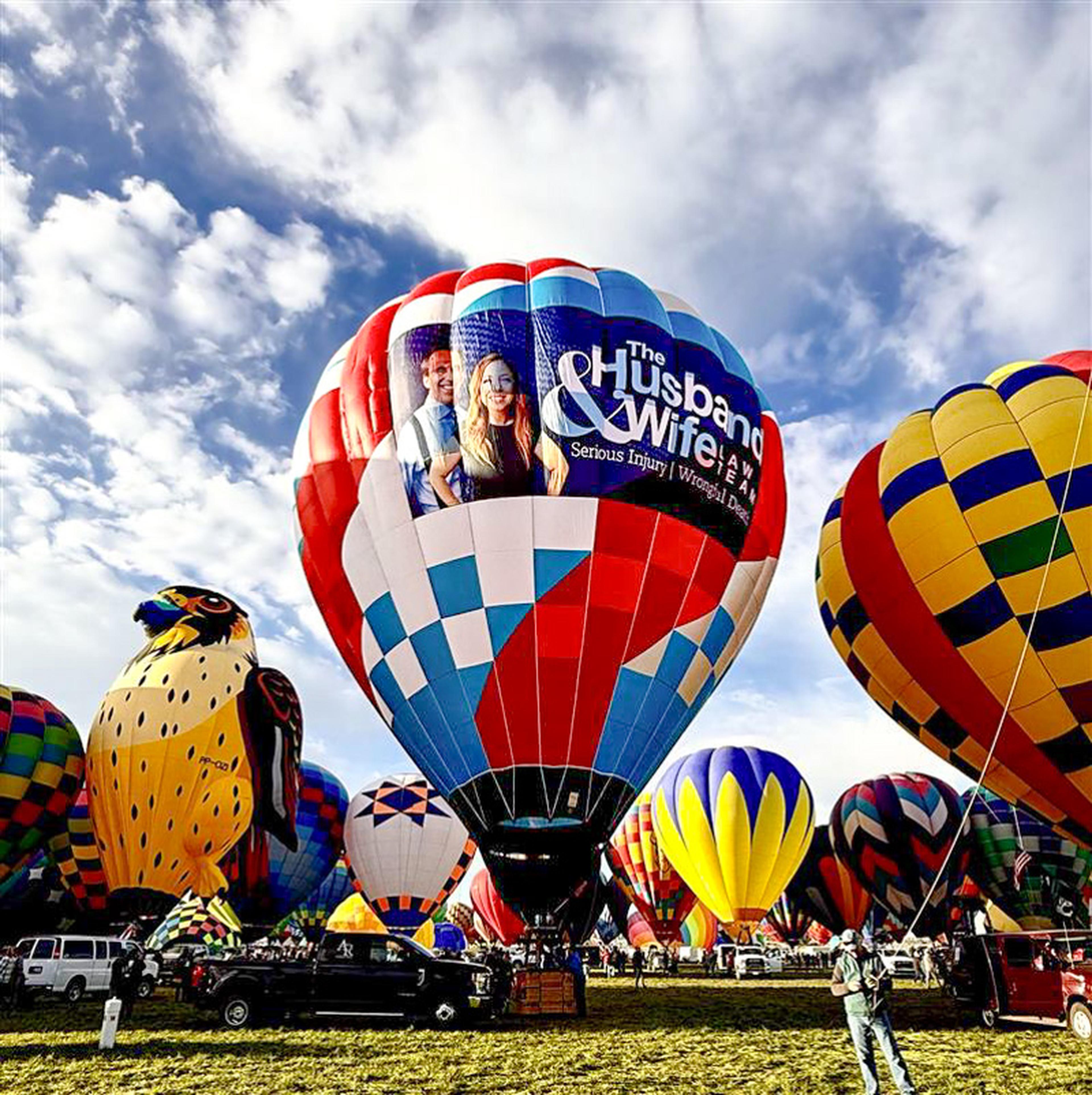 Colorful hot air balloons, including the Husband & Wife Law Team balloon, stand fully inflated and ready for flight at the Albuquerque International Balloon Fiesta.