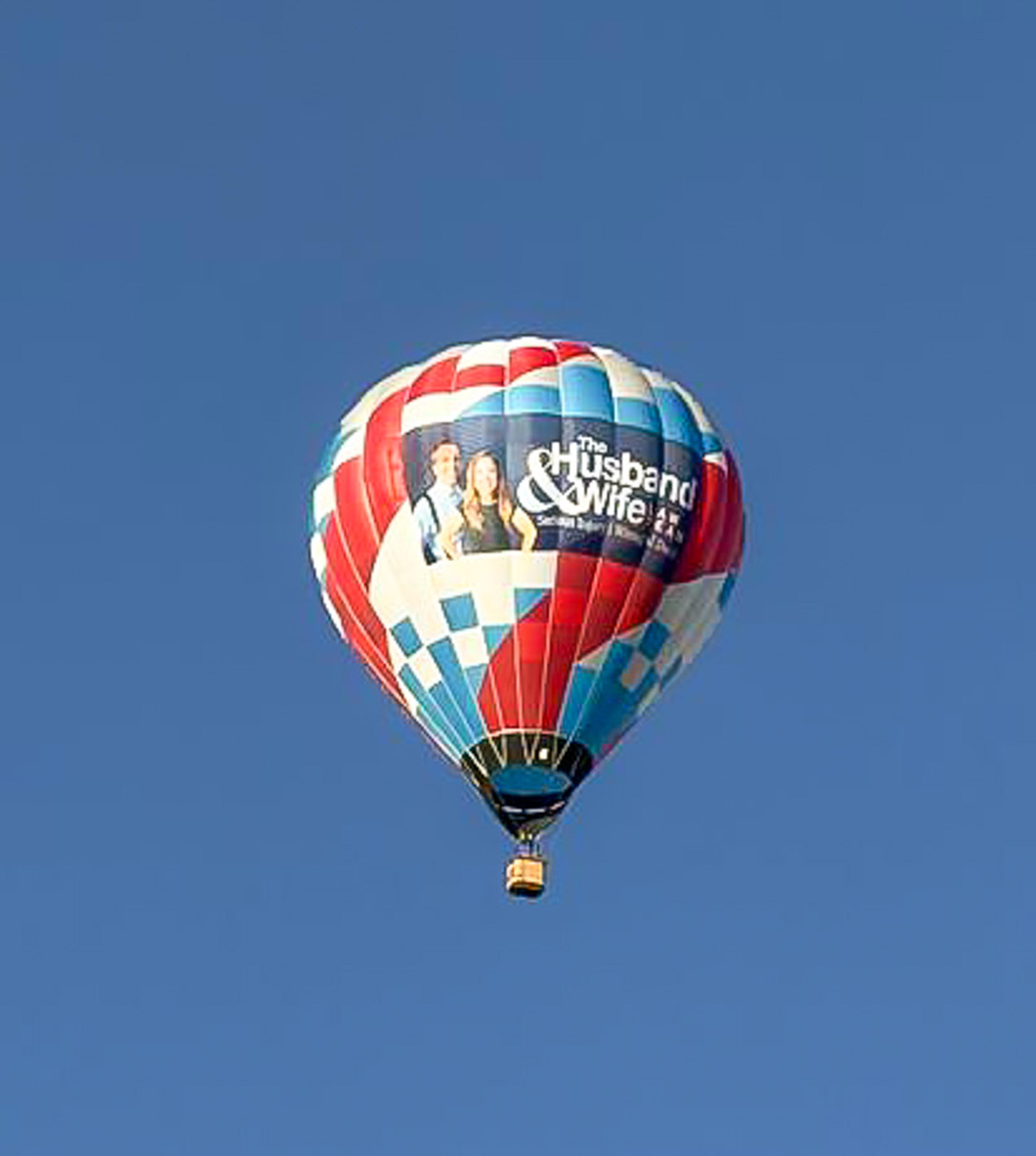 Flying high over Albuquerque! The vibrant Husband & Wife Law Team balloon stands out against the bright blue New Mexico sky.
