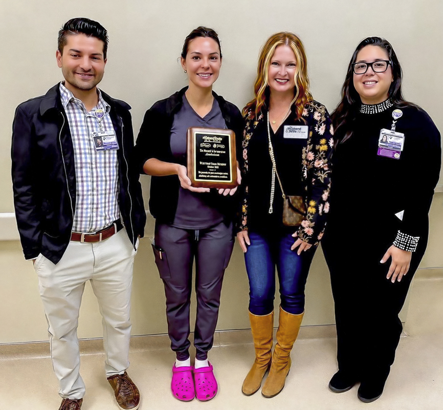 Nurse Cheyenne proudly holds her WOW Award as a Husband & Wife Law Team community representative and her coworkers celebrate her well-deserved recognition.