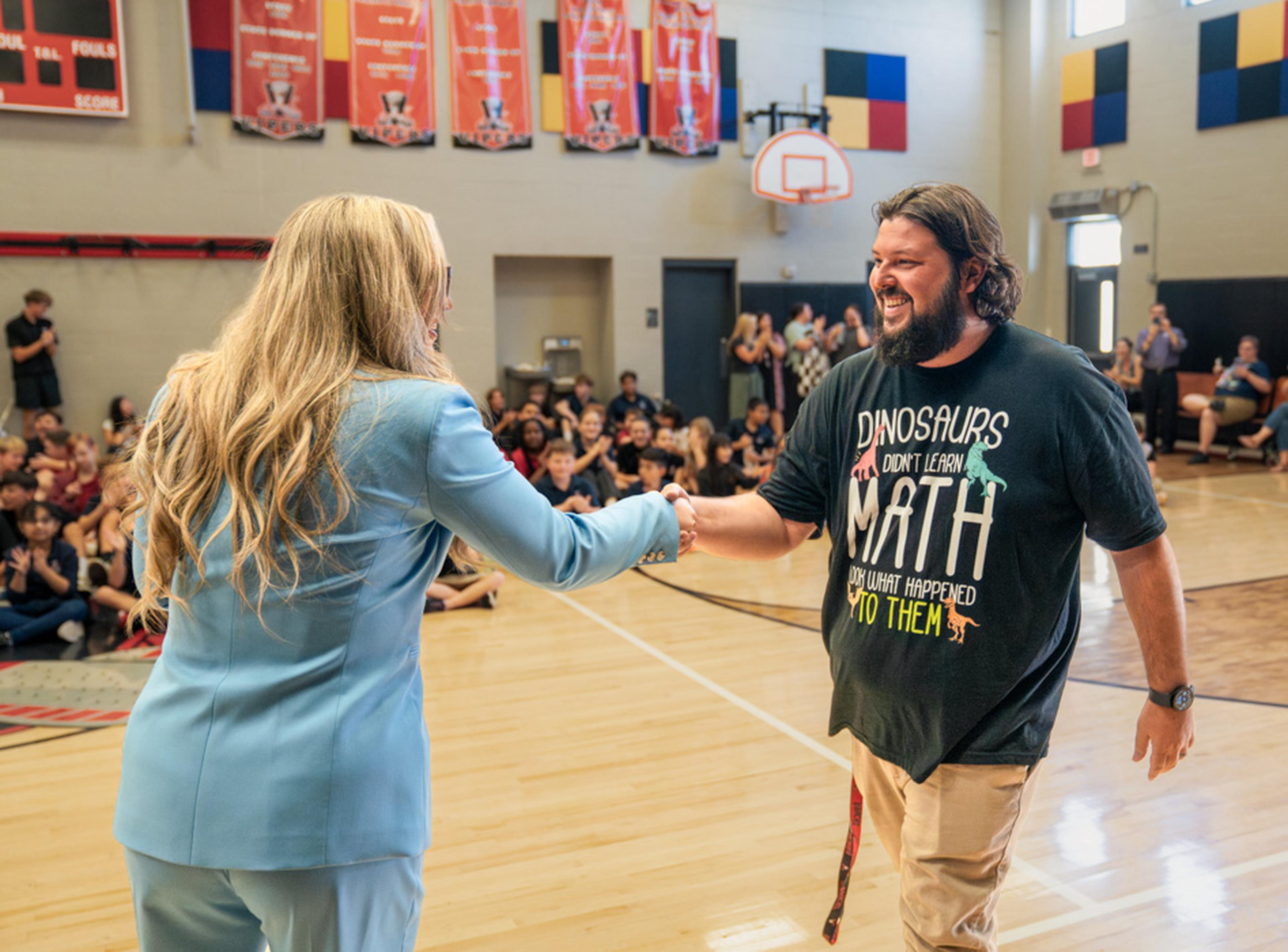 Jen from the Husband & Wife Law Team presents Mr. Knowles with the Teacher of the Month Award at Val Vista Academy, recognizing his dedication to students and education.