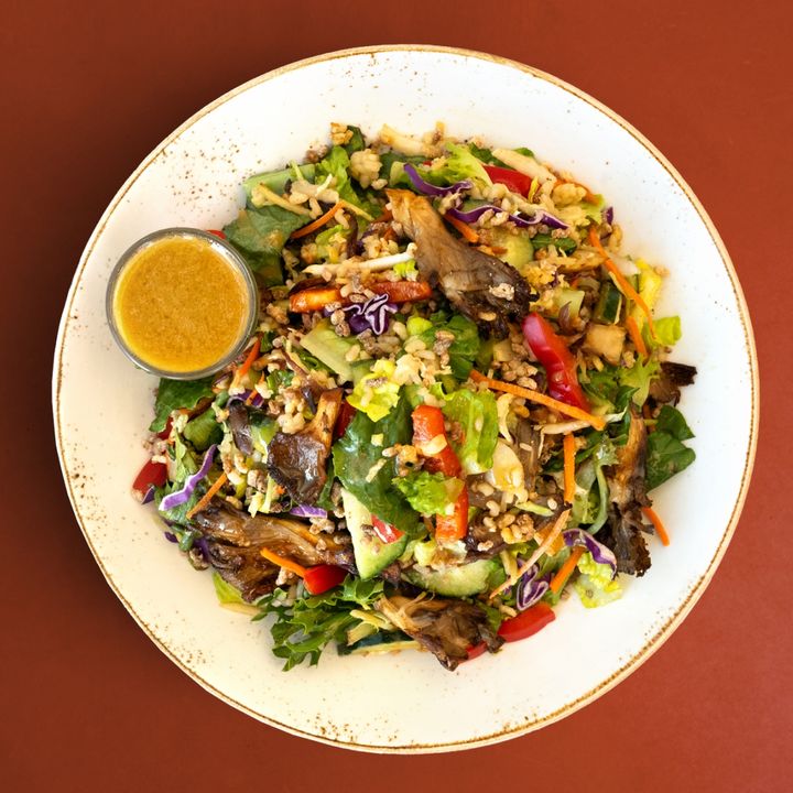 A colorful asian salad with lettuce, grains, vegetables, roasted mushrooms and crispy rice, served with vinaigrette dressing in Back Bay Boston