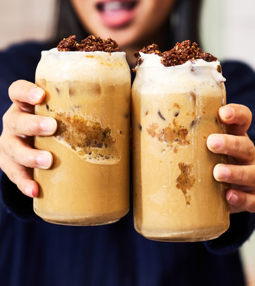 A person holding two glasses of iced coffee topped with vanilla cold foam and chocolate cookie crumbles.