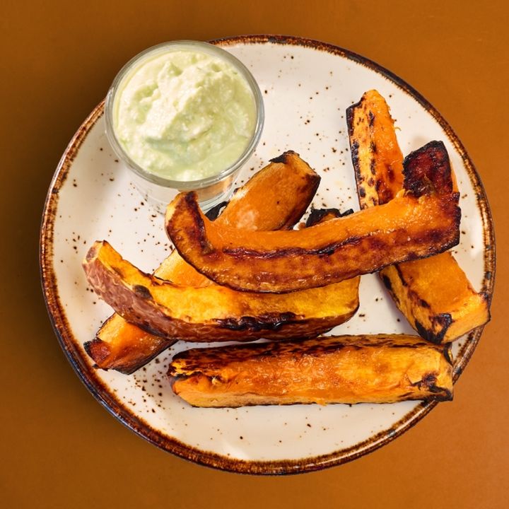 A plate of roasted koginut squash wedges with a side of spicy jalapeño dipping sauce.
