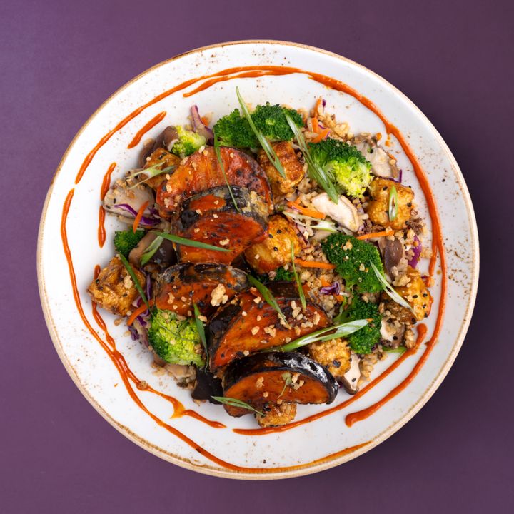 A colorful stir-fry with eggplant, broccoli, tofu, and sliced vegetables, garnished with sesame ginger sauce.