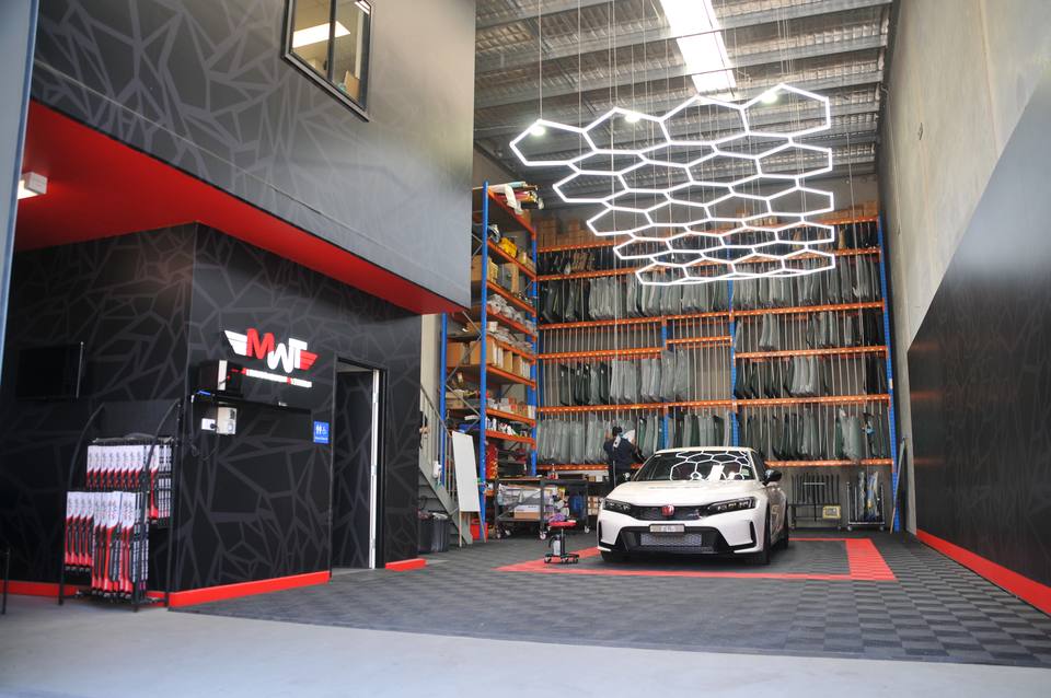Inside the MWT Auto Glass workshop at Warwick Farm, with windscreens racked behind a customer's car