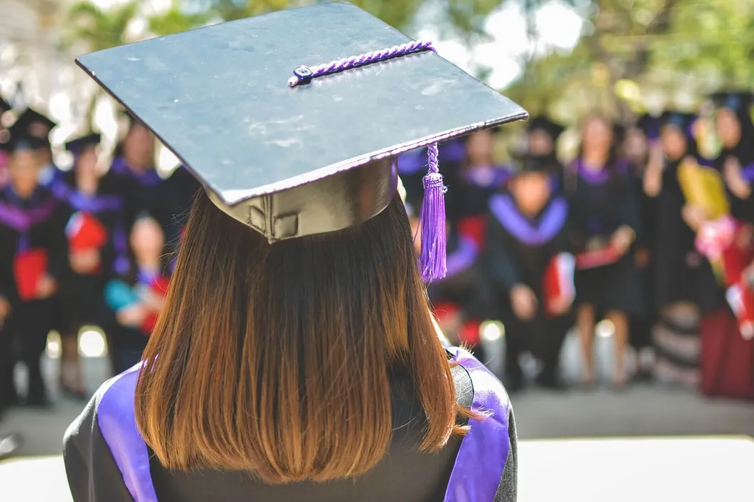 Graduate wearing cap and gown facing a crowd of other graduates