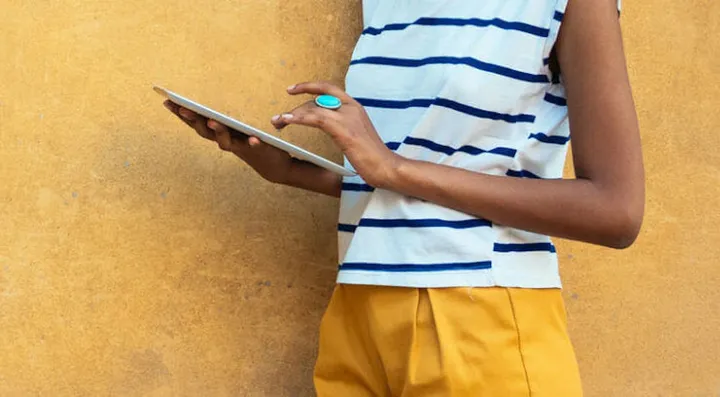 A woman in a striped shirt scrolls on an iPad in front of a yellow background