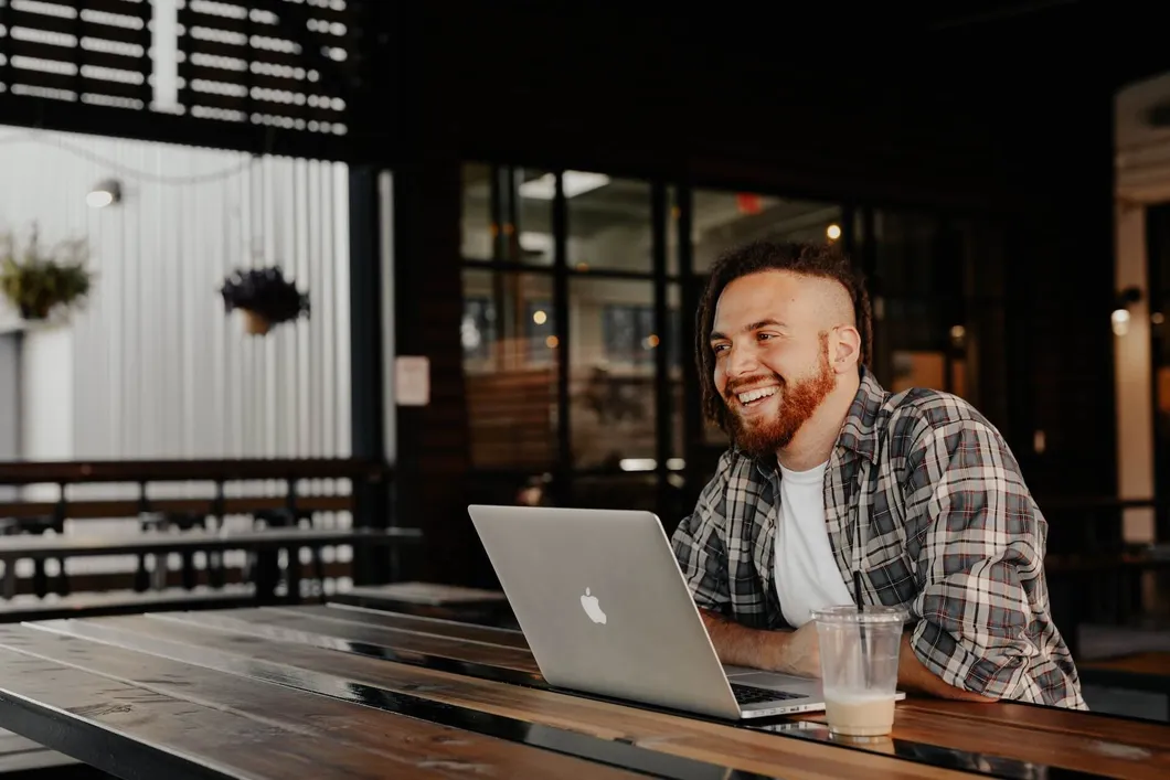 Man sitting in coffee shop smiling by himself with laptop