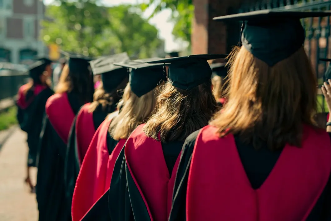 College graduates with black gowns and maroon scarves draped across their back.