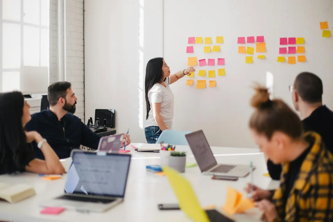 woman in a meeting standing in front of a whiteboard placing sticky notes on it