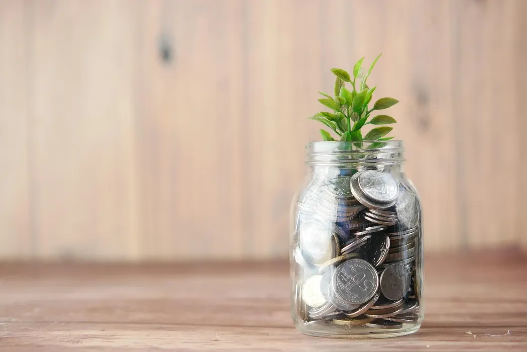 A mason jar with change in it and a plant growing out of it