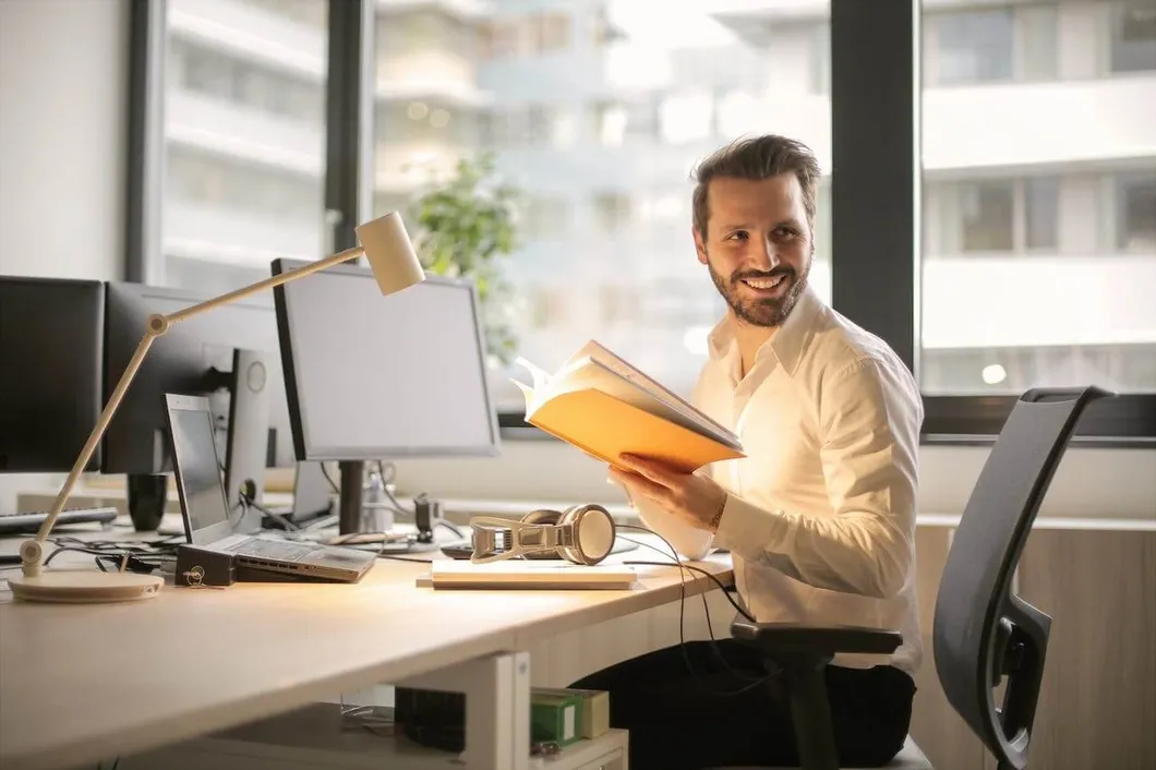 man-sitting-at-computer-desk-with-notebook-smiling