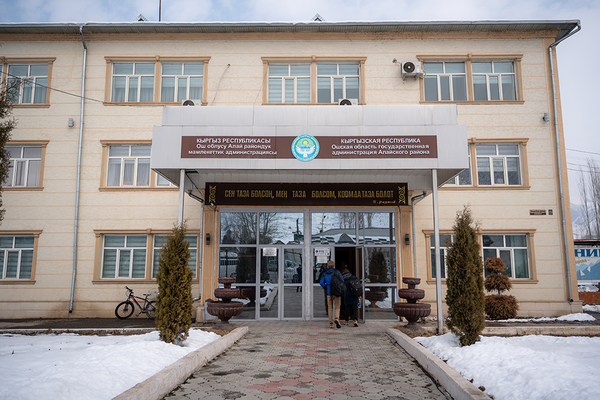 The entrance of a government building with Kyrgyz script, surrounded by snow-covered ground and bushes, with Notre Dame MBA students entering.