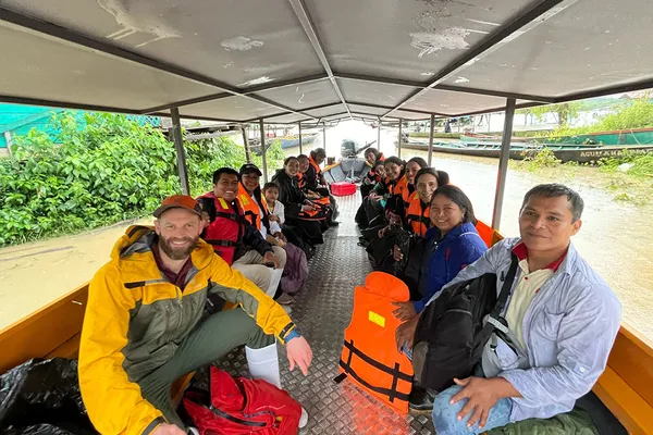 A group of people in colorful raincoats and life vests sit on a covered boat in the Peruvian Amazon, surrounded by lush greenery and water.