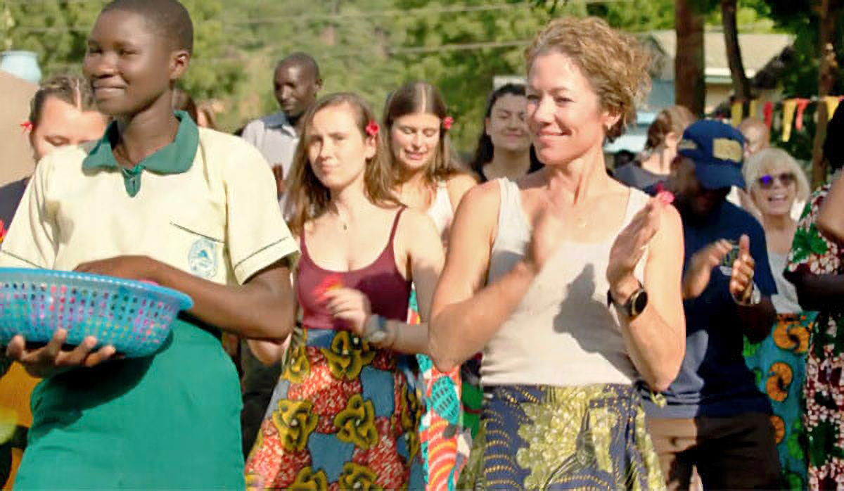 A group of diverse people joyfully walking outdoors, with some clapping and a person in front holding a blue basket.