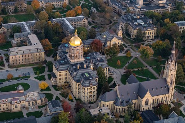 Ariel image of the main buliding & basilica on the University of Notre Dame campus.  The golden dome at the top of the main building shines in the sunlight.