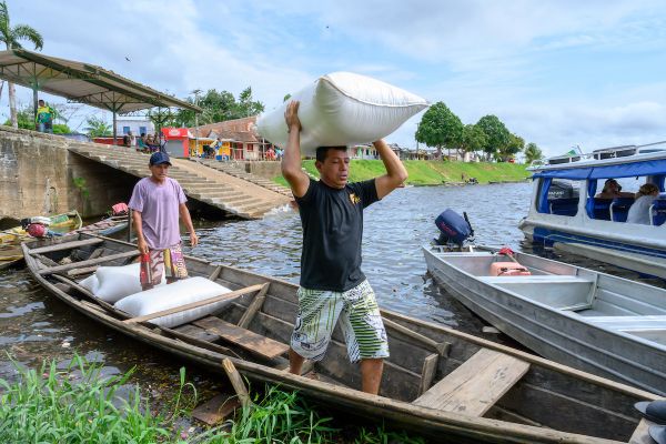 Two men load large bags of farina flour into a wooden canoe on the Amazon river in Brazil.