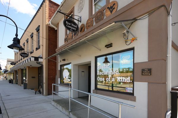 Street view of a shop with a sign "Bear Wood Company." The window displays "Rustic. Reclaimed. One of a Kind." Nearby are other storefronts.