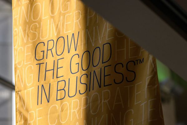 A gold banner near a window with Grow the Good In Business text on the banner in navy and other business words in light gold. The banner is in front of a window with sun shining on half and shadow on the other.