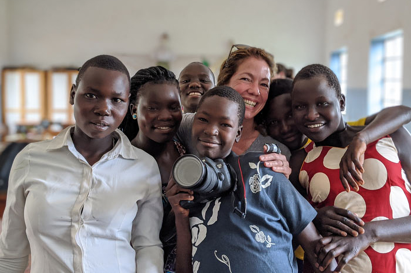 A group of smiling people, including a woman holding a camera, pose closely together indoors.