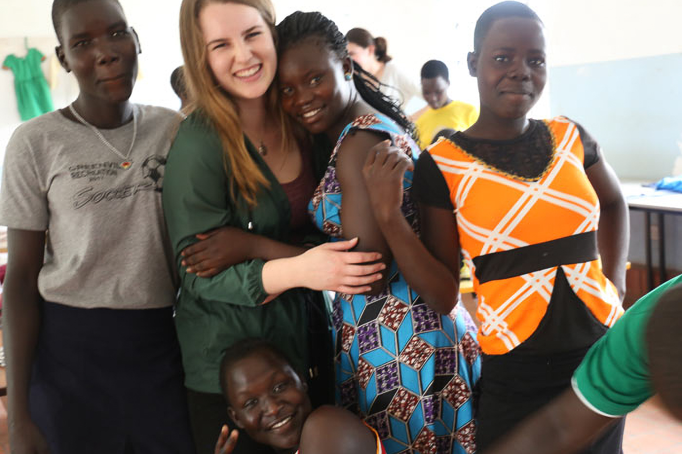 A group of smiling people, including a woman in a green shirt, pose closely together indoors, showcasing camaraderie and joy.