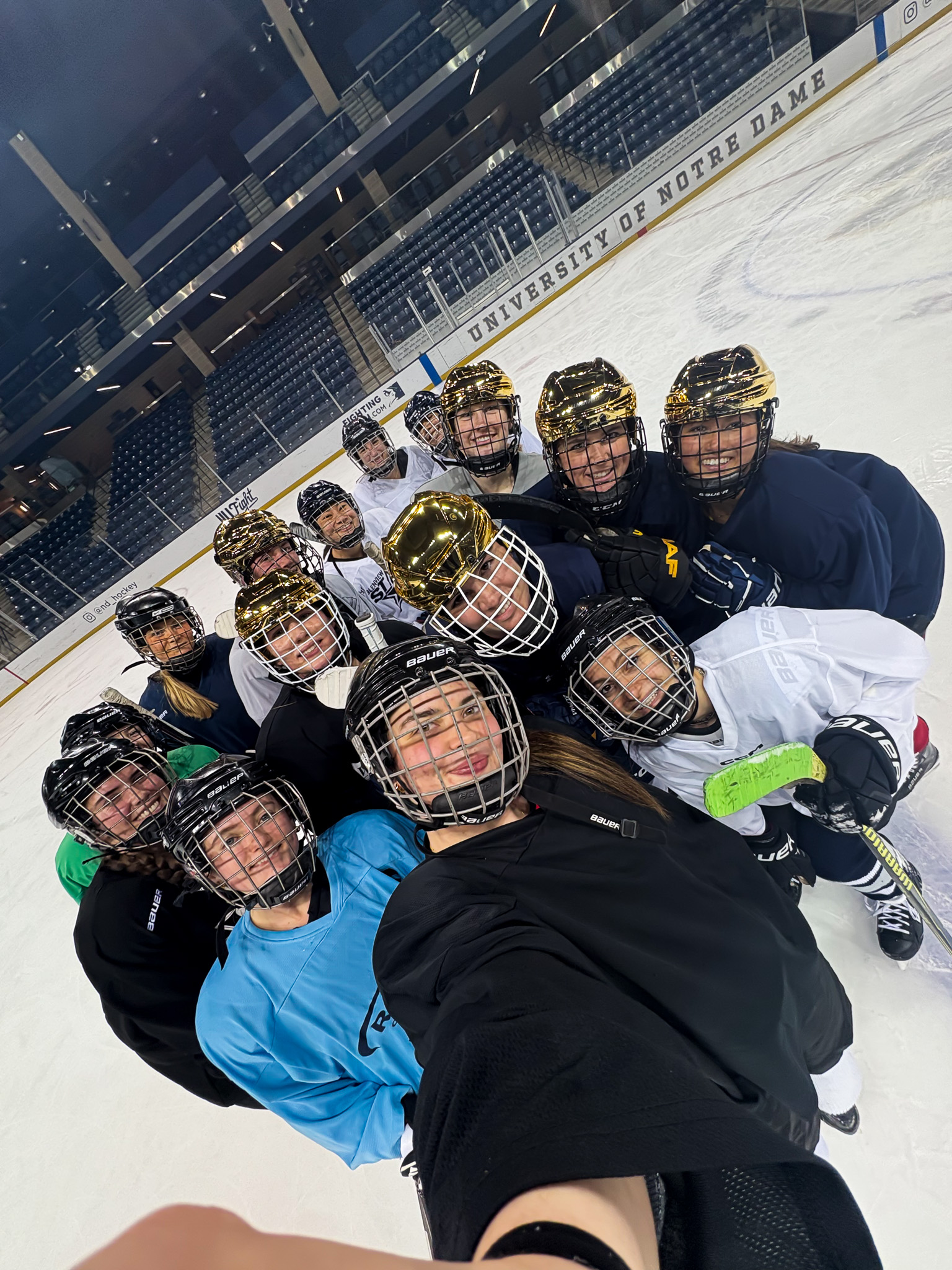 A group of ice hockey players wearing jerseys and helmets, taking a selfie on a rink at the University of Notre Dame.