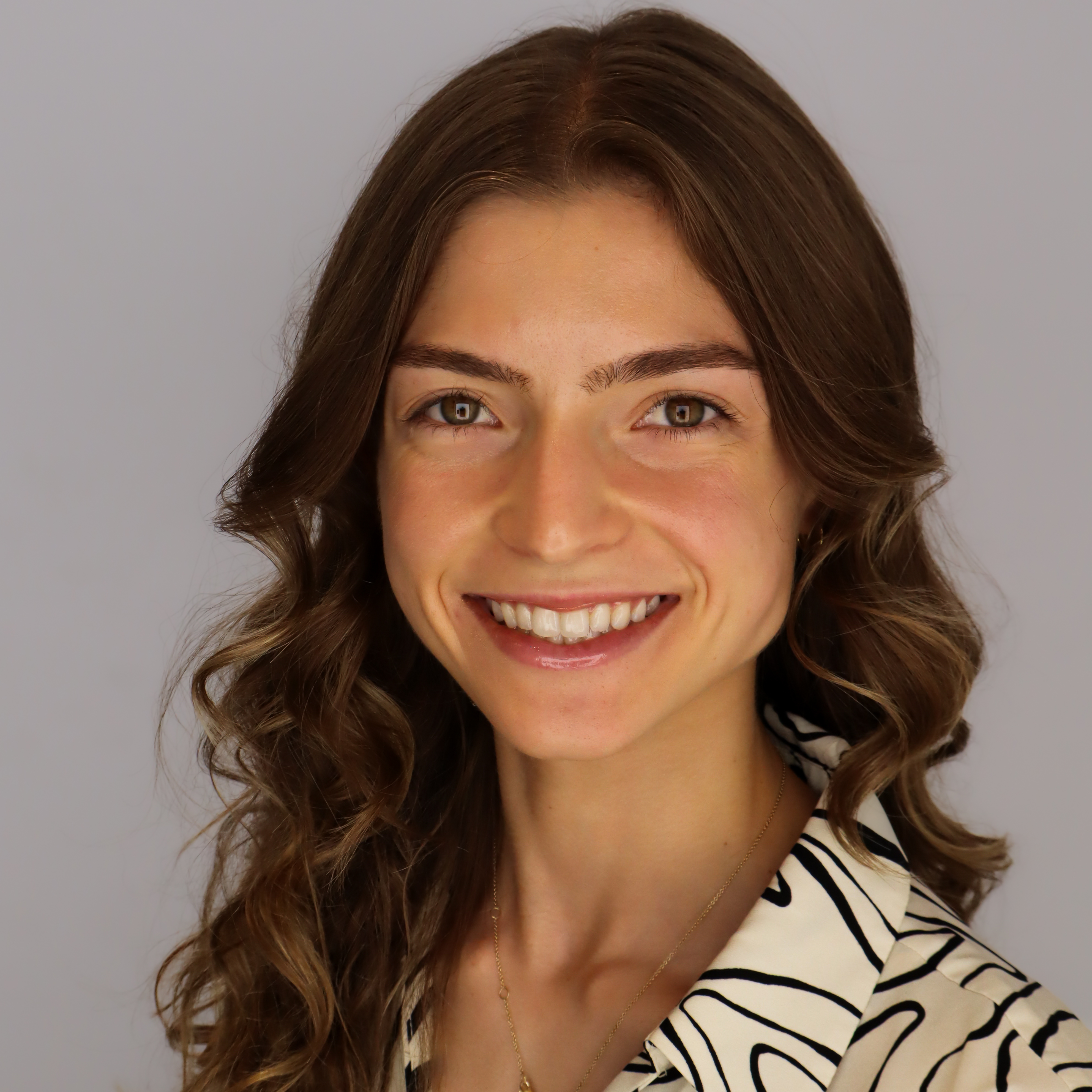 Smiling woman with long, wavy brown hair and a striped shirt against a plain background.