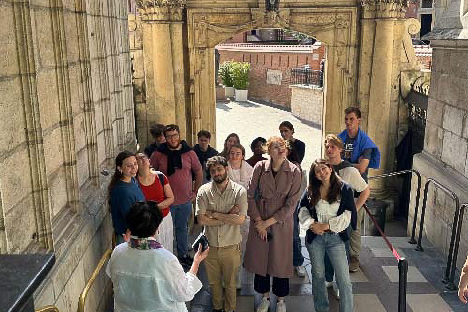 A group of people listens attentively to a guide inside a historical building with ornate stone architecture and an archway.