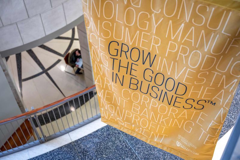 A gold banner with the words Grow the Good in Business and other business-related words on it hangs over the Mendoza atrium overlooking a student studying in the lower-level.