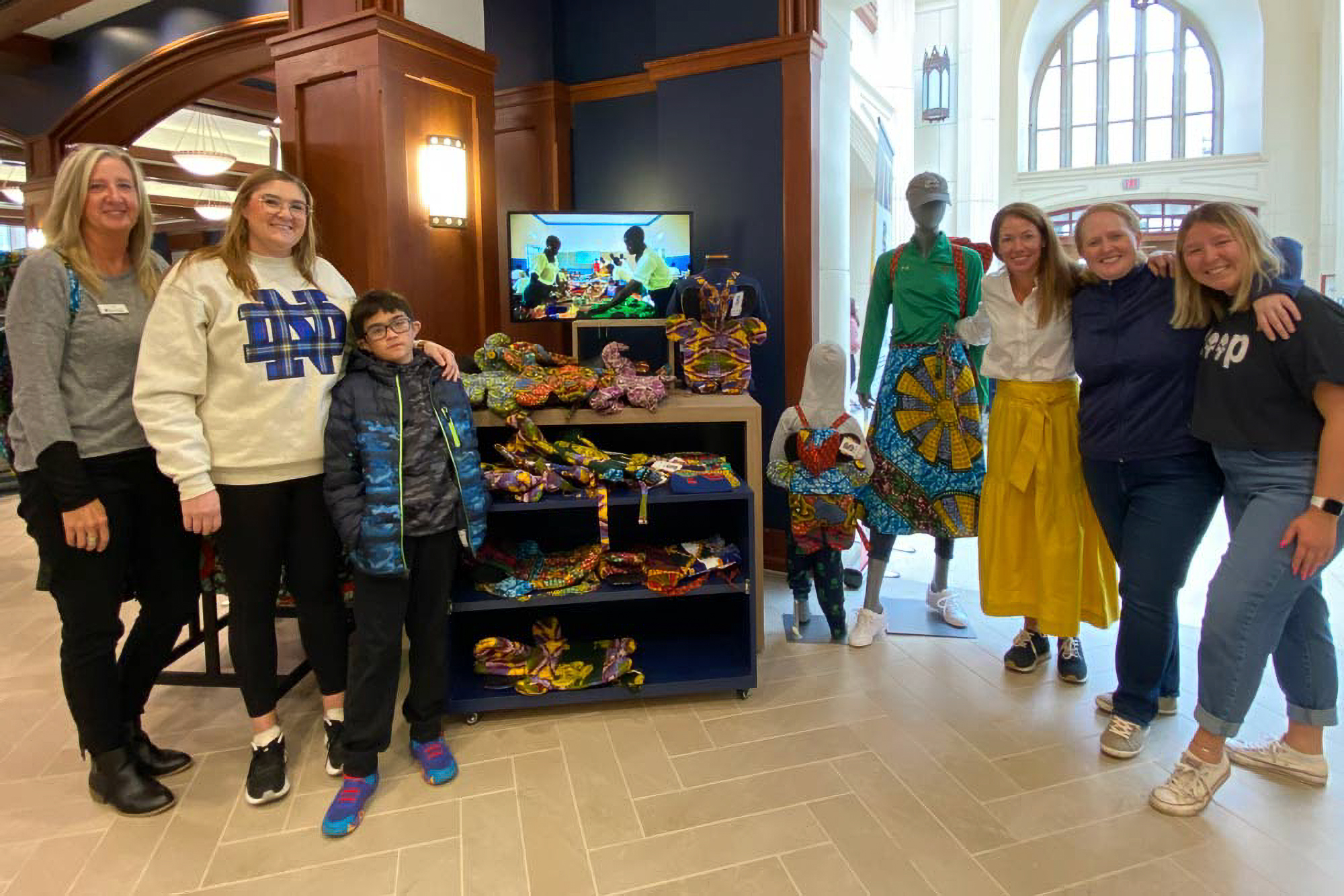 Group of people smiling next to a display of colorful clothing and accessories in a bright indoor setting.