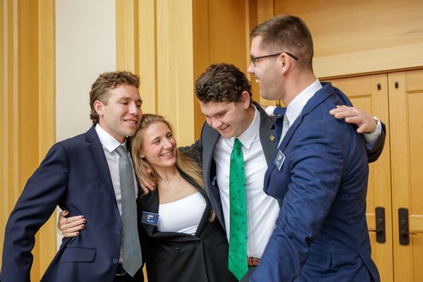 Four people in business attire stand huddled together, smiling warmly in a wooden-paneled atrium.
